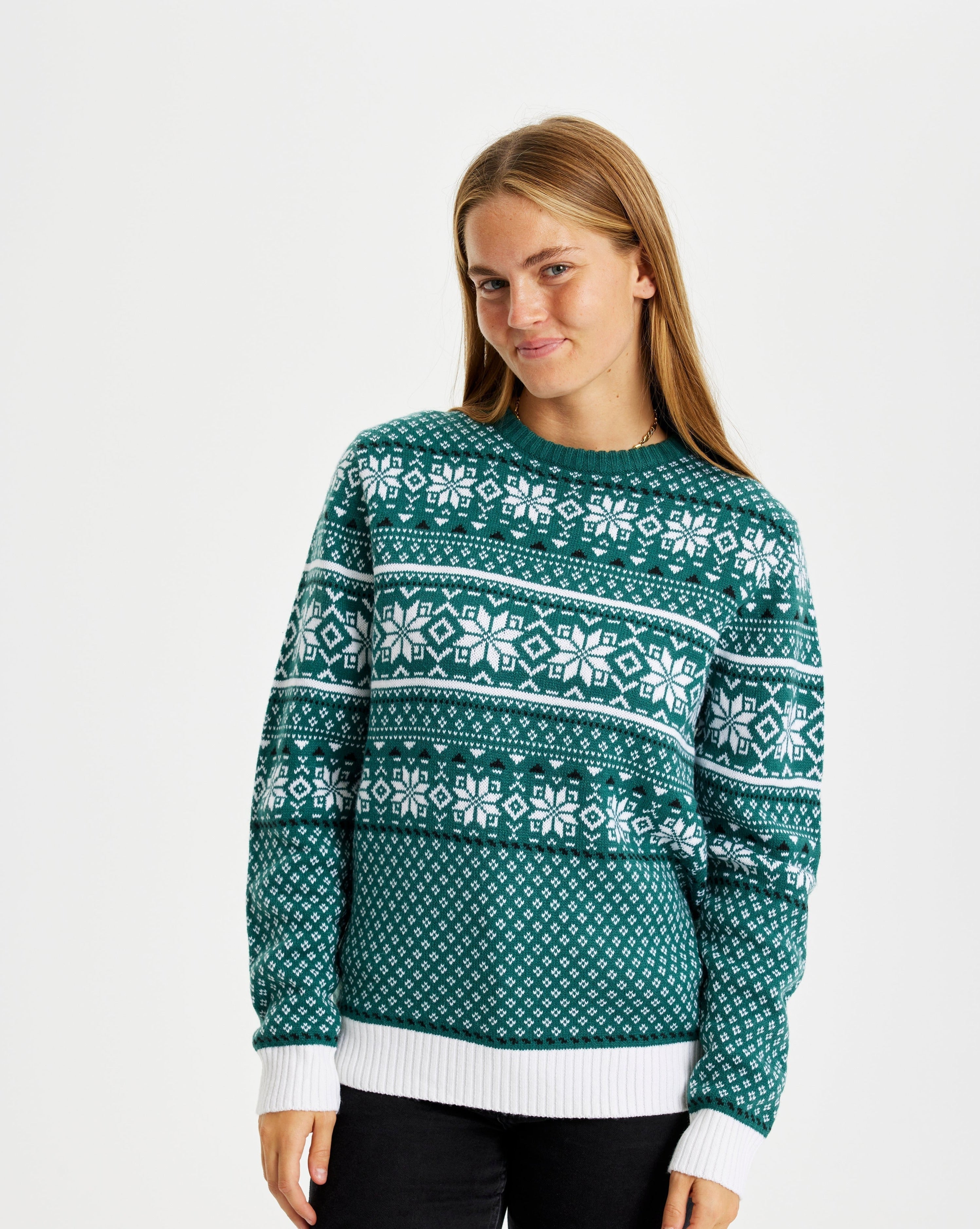 Une femme souriante portant un pull de Noël vert avec des flocons de neige.